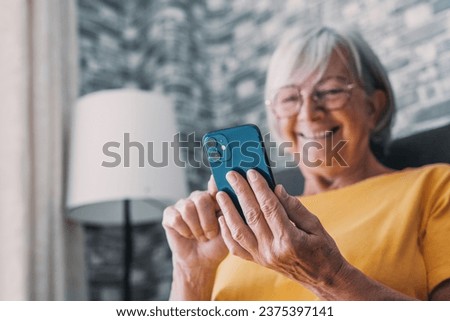 Smiling middle-aged Caucasian woman sit next to couch in living room browsing wireless Internet on phone, happy modern senior female relax on ground at home using smartphone device, elderly technology