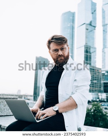 Portrait of male freelancer working on distance job at urban setting with skyscrapers on background