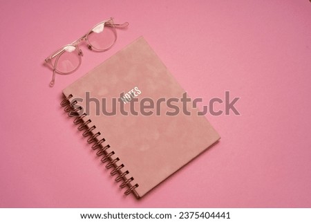 Business concept. Top view photo of workplace stack of pink planners pencils clips and white glasses on isolated pink background with blank space
