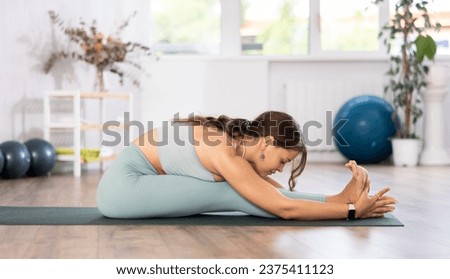 Skilled young female teacher demonstrating seated forward bend pose of yoga in training room Royalty-Free Stock Photo #2375411123