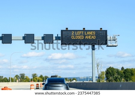 Overhead electronic highway sign, 2 left lanes closed ahead, on a sunny blue sky day

