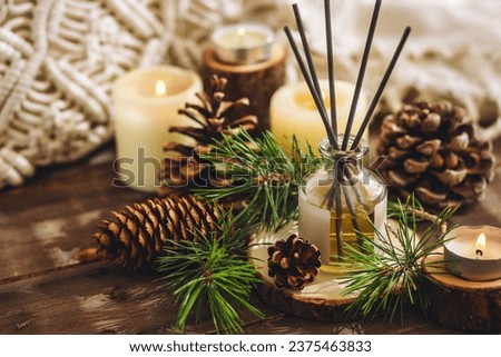 Christmas home aromatherapy. Aroma diffuser with pine extract, organic essential oil, cedar and spruce cone, candles on wooden table. Cozy atmosphere, holiday spirit. Winter inspiration and mood. Royalty-Free Stock Photo #2375463833