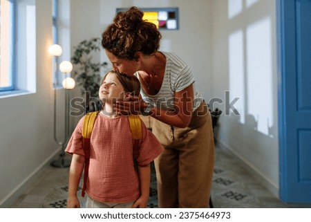 Curly haired mother kissing her daughter while helping her get ready for school in the morning