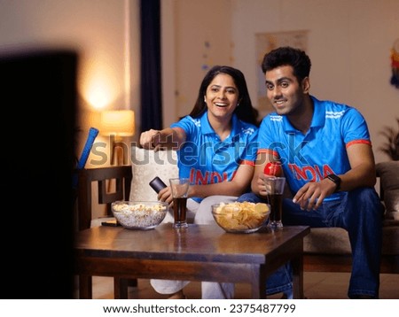 Indian man and a woman watching a live cricket match at home - World Cup match, 1-day match, Tense expression, T20 series. Couple wearing Indian jersey - face painted with Indian flag colors