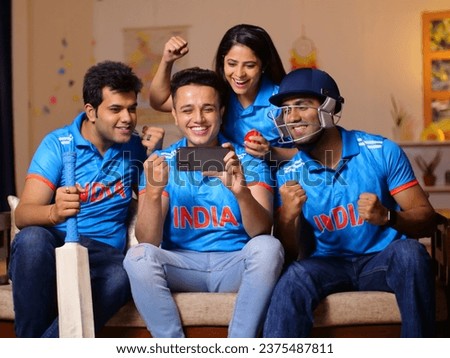 A group of fans in Indian jerseys sitting on couch and watching live cricket match on phone - cricket fever, . Indian cricket fans are engrossed in checking the live score, placing online bets