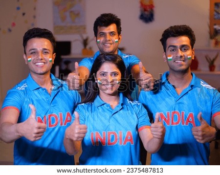 Indian friends dressed in Indian cricket team jersey posing for the camera - thumbs-up gesture, jersey with India's name, painted Indian flag. Indian friends in their cricket jerseys with the India...