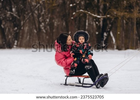 Brunette mother and and her daughter riding a sled in winter forest. High quality photo