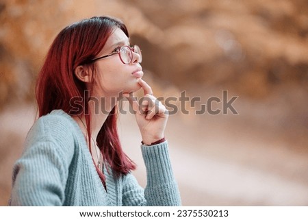 Portrait of red-haired teenage girl thinking with hand at her chin.