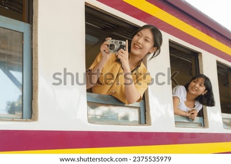 An Asian female tourist is capturing the joy of her friend as she leans out the train window.