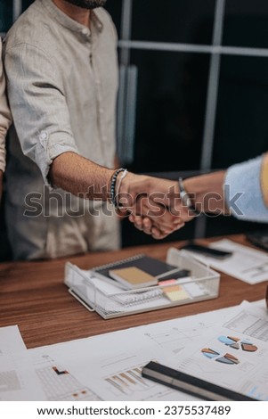 Multicultural colleagues bid farewell, embracing as one begins a new job. A touching moment of saying goodbye and shaking hands between business people indoors. Royalty-Free Stock Photo #2375537489