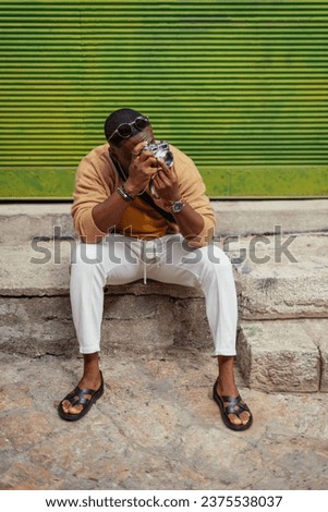 A young black guy is taking pictures while visiting the city