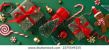 Holiday Setup: Overhead perspective of presents featuring charming bows, radiant red, green, and golden ornaments, gingerbread man tree decoration, tiny car transporting fir tree, candies on green