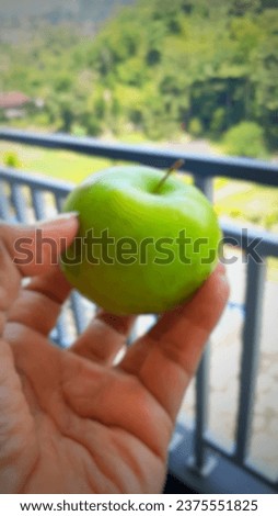 Defocused abstract background of Hand holding a green apple, with mountains in the background.