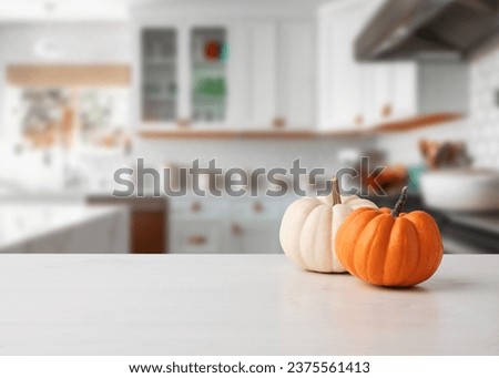 Autumn pumpkins on white wooden kitchen table pr counter with kitchen background.