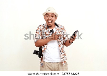 Wow excited expression of asian adult man tourist standing while holding and pointing a cell phone. Concept of travel. Isolated on white background