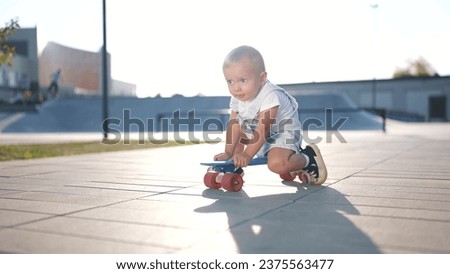 baby rides sitting on a skateboard. happy family kid dream concept. baby son learning to skateboard playing funny video. child in a skate park rides skateboard outdoors lifestyle