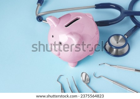 Pink piggy bank with dentist tools on blue background, copy space Royalty-Free Stock Photo #2375564823