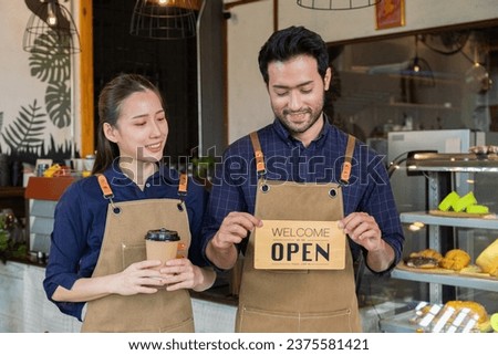 Small business couple husband and wife startup lifestyle concept, Asian man and woman wearing apron standing in front of counter holding coffee cup and open sign, coffee shop owner partnership.