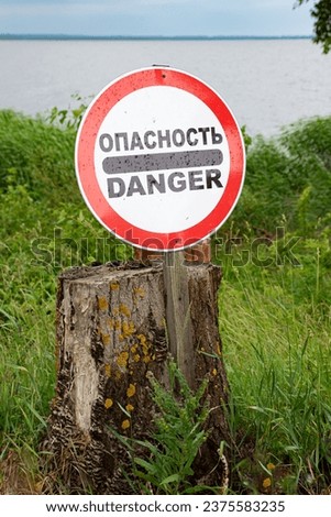 Warning sign "Danger" in English and Russian. A sign on the shore.
