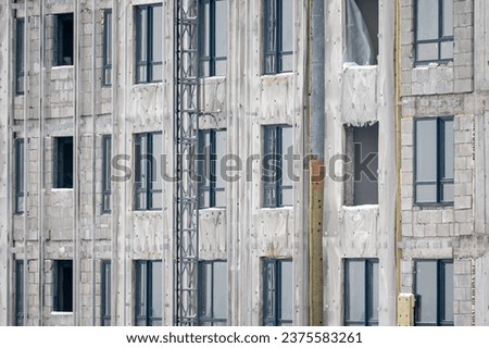 Construction of a new house. View of a fragment of an unfinished building made of gray concrete with multi-storey windows without glass. The concept of building and housing provision. Royalty-Free Stock Photo #2375583261