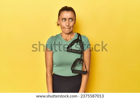 Middle aged sportswoman with resistance band on yellow confused, feels doubtful and unsure.