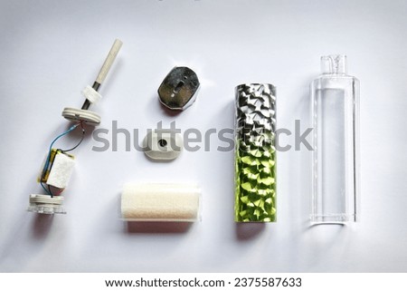 The components of a discarded neon single use electronic cigarette vape are laid out on a white paper surface, showing the battery, shell, mouthpiece, and vape liquid parts    Royalty-Free Stock Photo #2375587633