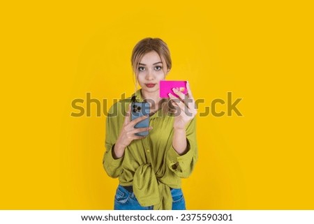 Woman hold credit bank card, young beautiful blonde woman hold credit bank card. Standing over yellow studio background. Hold mobile phone. 20s caucasian girl offer online shopping, payment concept.
