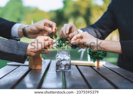 Business people put coin to money saving glass jar on outdoor table as sustainable money growth investment or eco-subsidize. Green corporate promot and invest in environmental awareness. Gyre Royalty-Free Stock Photo #2375595379
