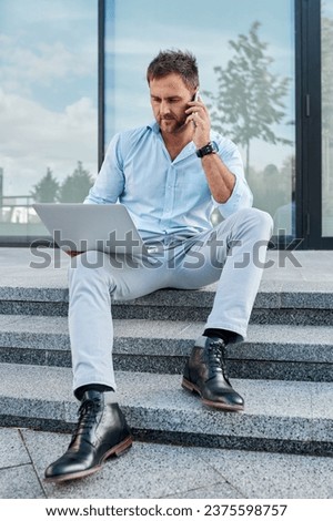 Caucasian man studying business proposal using laptop while sitting on the street.