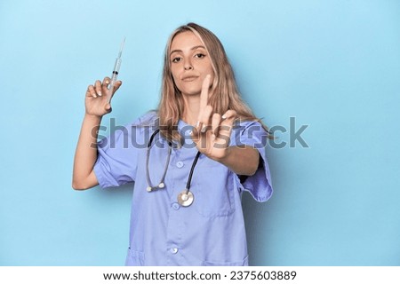 Young caucasian nurse in blue studio showing number one with finger.