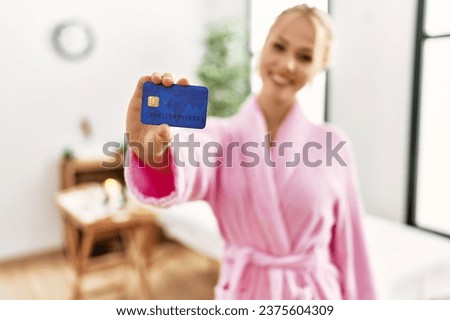 Young caucasian woman wearing bathrobe holding credit card at beauty salon