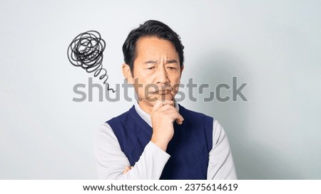 A middle-aged Asian man wearing a casual wear showing a depressed expression in front of a blue background. Royalty-Free Stock Photo #2375614619