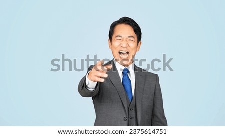 Asian middle-aged man in a business suit laughing in front of a blue background. Royalty-Free Stock Photo #2375614751