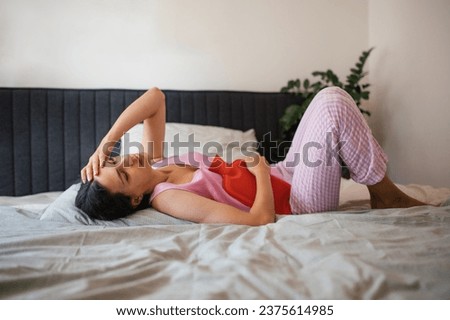 Woman at home suffering from menstrual pain. Menstrual cramps, woman warming lower abdomen with a hot water bottle, endometriosis, and diseases causing pain. Royalty-Free Stock Photo #2375614985
