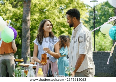 Friends talking and having fun at summer grill garden party. Multiracial couple hosting garden party.