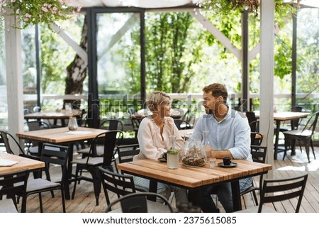 Beautiful couple in a restaurant, on romantic date. Wife and husband kissing, having romantic moment at restaurant patio.
