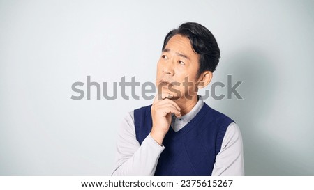 Thoughtful middle-aged Asian man wearing casual wear in white background. Royalty-Free Stock Photo #2375615267