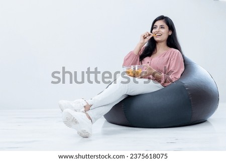 Happy Beautiful Female sitting on Bean bag and having chips snacks watching Movies on Isolated background