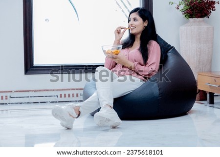 Happy Beautiful Female sitting on Bean bag and having chips snacks watching Movie