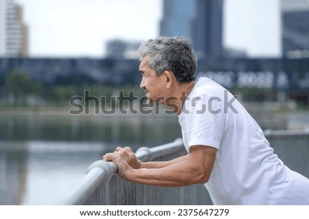 older adult male stretching arms walkway steel railing by the pond in the city,healthy senior man with grey hair warming up before exercise, concept of elderly people lifestyle, healthcare, wellbeing