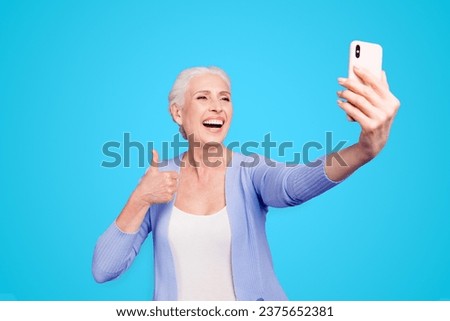 Grey haired old happy excited funny funky woman wearing casual, taking self picture, showing thumb up, opened mouth. Isolated over violet purple background