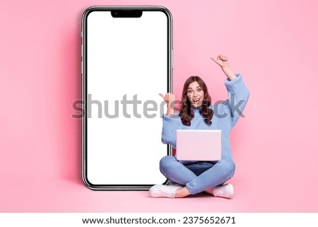 Full length photo of excited cheerful person sit floor use netbook direct fingers empty space billboard isolated on pink color background