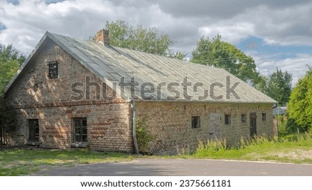 Historic brick farm building under a cloudy blue sky.An old historic building made of white and red bricks with a sloping tin roof and a visible brick chimney. Royalty-Free Stock Photo #2375661181