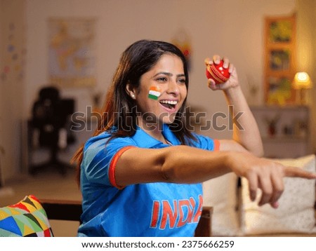 Closeup shot of a young Indian woman celebrating the Indian cricket team's victory - watching a live cricket sports match on TV. Female Indian cricket fan wearing an Indian jersey - cheering