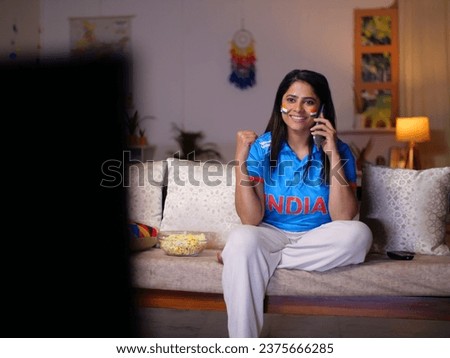 Young Indian woman celebrating Indian cricket team's victory - watching live cricket sports match on TV.. Female Indian cricket fan wearing an Indian jersey - excitement, cheering for team, female ...