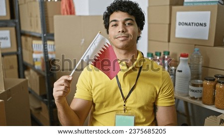 Young latin man volunteer holding qatar flag smiling at charity center