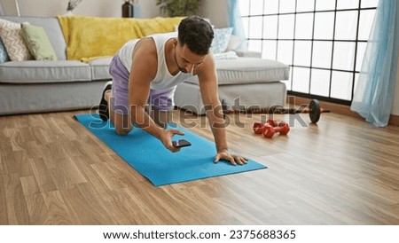 Young arab man sitting on yoga mat using smartphone at home