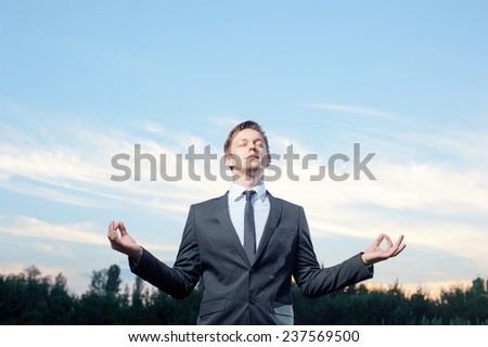 Businessman meditating outdoor. Relaxed young caucasian man in formalwear meditating while standing with sunset in the background