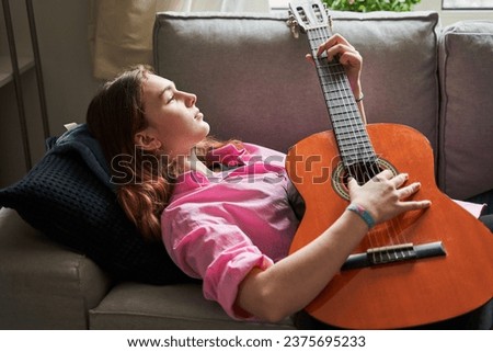 Portrait of pensive young woman playing guitar and dreaming