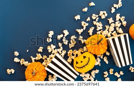 Jack o lantern,decorative pumpkins and striped boxes with popcorn on a blue background. TV watching concept with copy space. Movie night. Entertainment concept.